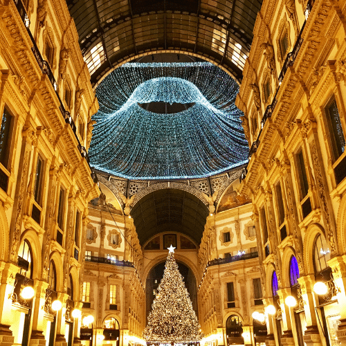 Weihnachtlich geschmückt ist die Galerie in Mailand. In der Mitte steht ein großer beleuchteter Tannenbaum, darüber and er Decke eine riesiges Lichterkettennetz. Umgeben von den luxuriösen Geschäften der Galerie.