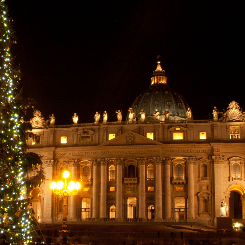 Zu sehen ist der Vatikan in Rom, nachts. Auf der Linken Seite ist ein mit Lichterketten verzierten Weihnachtsbaum.